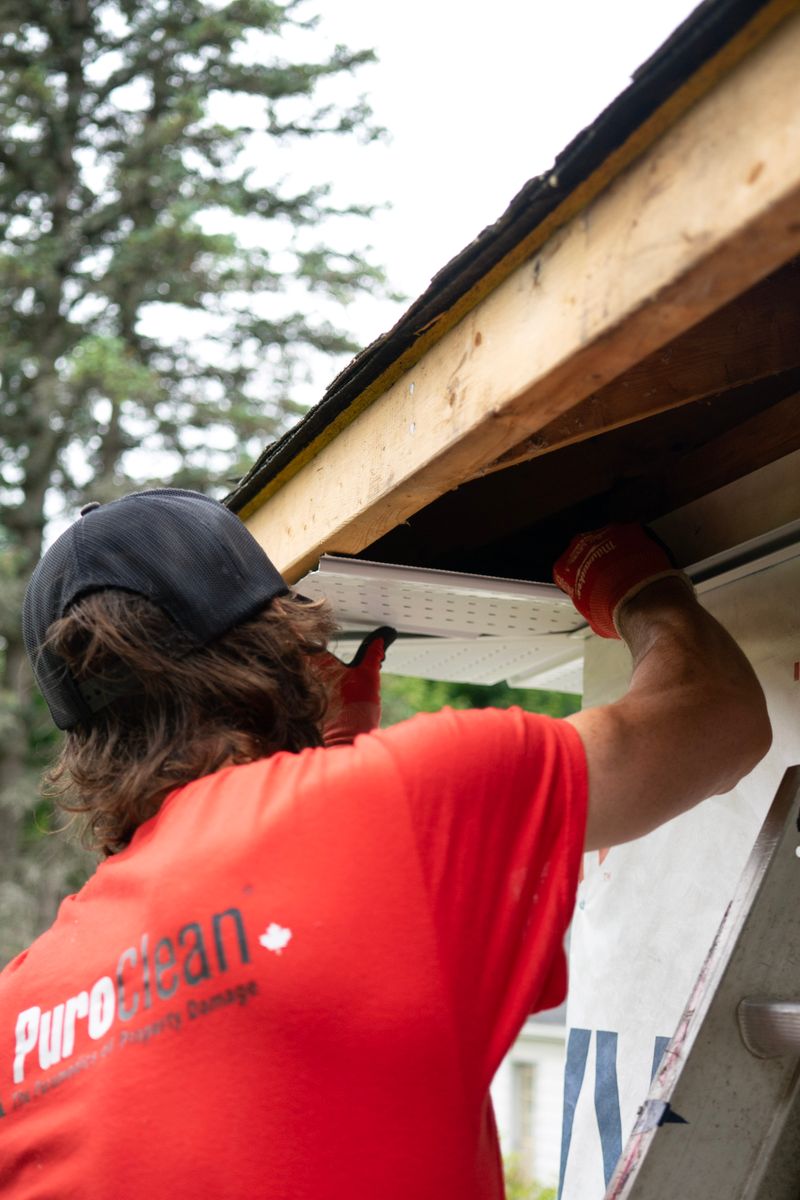 Worker fitting a gutter under a roof